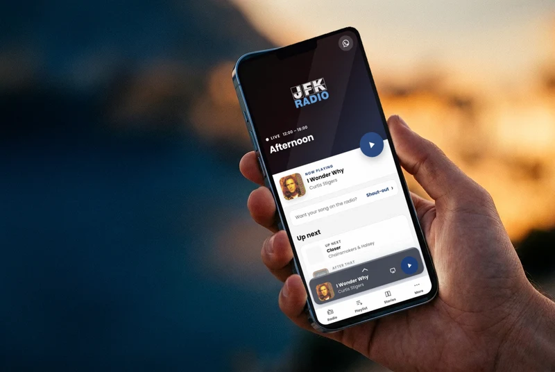 A hand holding a phone with the JFK Radio app